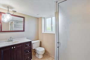 Bathroom with a shower with door, a textured ceiling, toilet, vanity, and tile patterned flooring