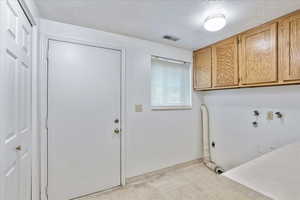 Clothes washing area with hookup for an electric dryer, a textured ceiling, and cabinets