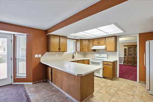 Kitchen featuring kitchen peninsula, light tile patterned floors, a textured ceiling, sink, and white appliances