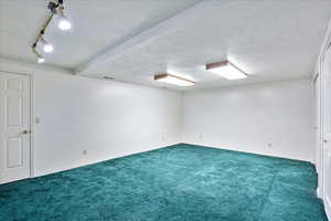 Carpeted spare room featuring beam ceiling, track lighting, and a textured ceiling