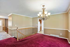 Carpeted spare room with ornamental molding, a notable chandelier, and a textured ceiling