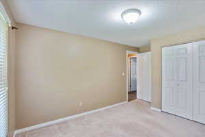 Unfurnished bedroom with a closet, a textured ceiling, and light colored carpet