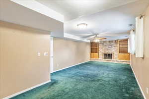 Unfurnished living room featuring a textured ceiling, a brick fireplace, ceiling fan, carpet, and built in shelves