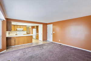 Kitchen featuring white appliances, sink, a textured ceiling, kitchen peninsula, and light carpet