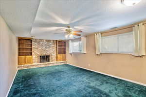 Unfurnished living room featuring a fireplace, a textured ceiling, built in features, and carpet floors