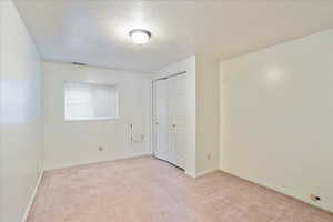 Unfurnished bedroom with light carpet, a textured ceiling, and a closet