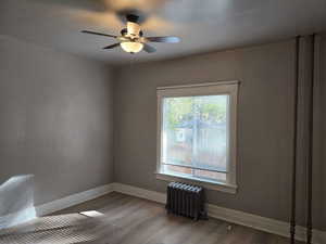 Unfurnished room featuring ceiling fan, wood-type flooring, and radiator heating unit