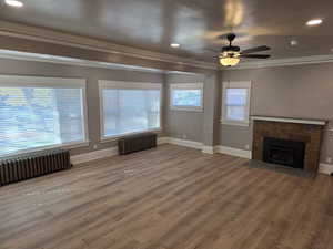 Unfurnished living room featuring radiator, ceiling fan, crown molding, and hardwood / wood-style floors