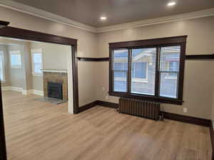 Unfurnished living room featuring light hardwood / wood-style flooring, ornamental molding, radiator heating unit, and a tile fireplace