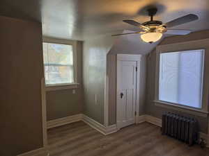 Additional living space featuring ceiling fan, wood-type flooring, and radiator heating unit