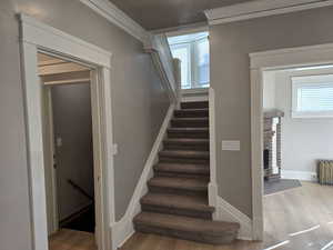 Stairs with radiator, hardwood / wood-style flooring, ornamental molding, and a brick fireplace