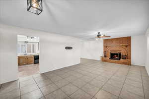 Unfurnished living room with sink, a brick fireplace, light tile patterned floors, a textured ceiling, and ceiling fan