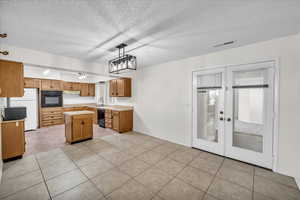 Kitchen with black appliances, sink, a textured ceiling, a center island, and decorative light fixtures