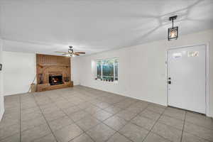 Unfurnished living room with ceiling fan, a textured ceiling, light tile patterned floors, and a fireplace