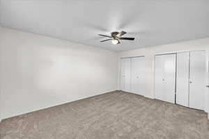 Unfurnished bedroom featuring ceiling fan, light carpet, and two closets