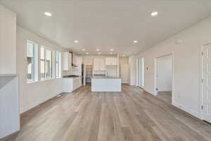 Kitchen featuring wall chimney range hood, a center island with sink, sink, white cabinetry, and light hardwood / wood-style floors