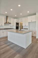 Kitchen featuring white cabinets, an island with sink, stainless steel appliances, wall chimney exhaust hood, and sink