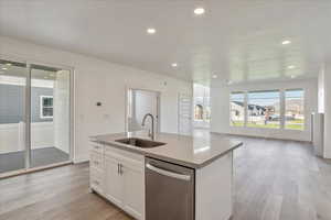 Kitchen with dishwasher, a kitchen island with sink, sink, light wood-type flooring, and white cabinets