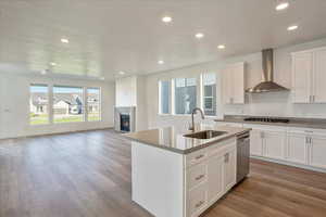 Kitchen with dishwasher, sink, wall chimney exhaust hood, white cabinets, and a center island with sink