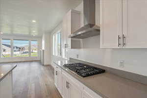 Kitchen with white cabinets, light hardwood / wood-style floors, wall chimney range hood, and stainless steel gas stovetop