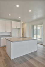 Kitchen featuring an island with sink, sink, light wood-type flooring, white cabinets, and a textured ceiling