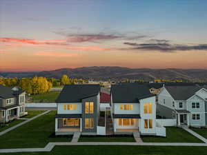 Back house at dusk featuring a mountain view and a lawn