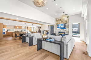 Living room featuring a stone fireplace, light hardwood / wood-style flooring, a chandelier, and a towering ceiling