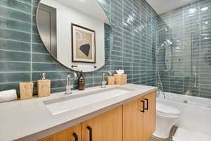 Full bathroom featuring decorative backsplash, toilet, vanity, bath / shower combo with glass door, and tile walls