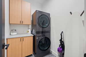 Clothes washing area with cabinets, light tile patterned floors, and stacked washer and clothes dryer