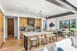 Kitchen featuring a center island with sink, backsplash, decorative light fixtures, and light wood-type flooring