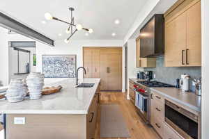 Kitchen featuring appliances with stainless steel finishes, a kitchen island with sink, light hardwood / wood-style floors, wall chimney exhaust hood, and sink