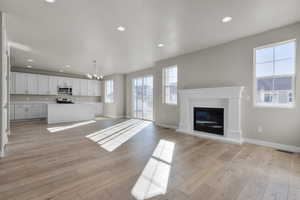 Unfurnished living room featuring a notable chandelier, a healthy amount of sunlight, and light wood-type flooring