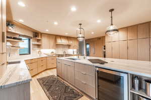 Kitchen featuring tasteful backsplash, hanging light fixtures, beverage cooler, light stone countertops, and light brown cabinetry