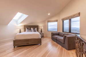 Bedroom with a mountain view, vaulted ceiling with skylight, and light wood-type flooring