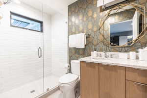 Bathroom featuring a shower with door, vanity, and toilet