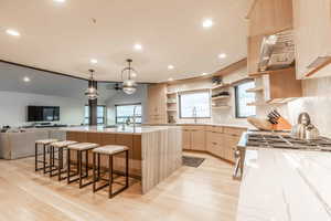 Kitchen featuring a center island with sink, extractor fan, light brown cabinetry, light hardwood / wood-style flooring, and pendant lighting