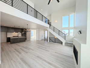 Unfurnished living room with a high ceiling, light wood-style flooring, stairs, a ceiling fan, and baseboards