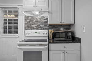 Kitchen with white range with electric stovetop, white cabinets, dark stone counters, and tasteful backsplash