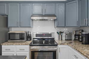 Kitchen with blue cabinetry, stainless steel appliances, light stone counters, and white cabinets