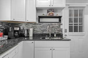 Kitchen featuring dishwasher, decorative backsplash, dark stone countertops, sink, and white cabinetry