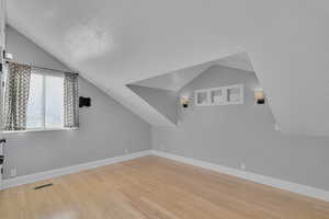 Additional living space with a textured ceiling, vaulted ceiling, and light wood-type flooring