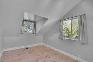 Bonus room with vaulted ceiling, a textured ceiling, and light wood-type flooring