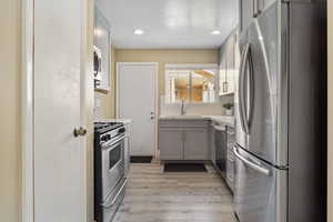 Kitchen with backsplash, sink, gray cabinetry, light hardwood / wood-style floors, and stainless steel appliances