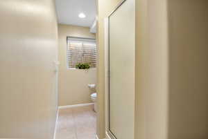 Bathroom with a shower with door, toilet, and tile patterned flooring