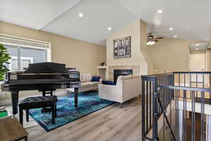 Living room featuring lofted ceiling, a tiled fireplace, light wood-type flooring, and ceiling fan