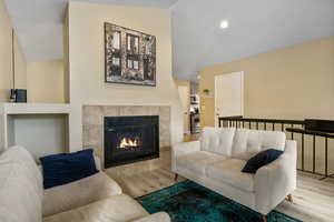 Living room featuring a tiled fireplace, lofted ceiling, and light hardwood / wood-style flooring