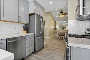 Kitchen with lofted ceiling, backsplash, appliances with stainless steel finishes, light wood-type flooring, and gray cabinets