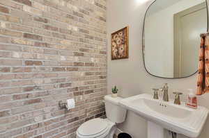 Bathroom with toilet, brick wall, and sink