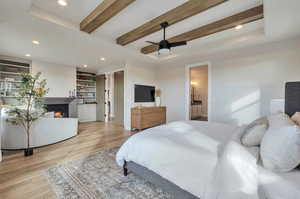 Bedroom featuring ensuite bath, beamed ceiling, light hardwood / wood-style floors, and ceiling fan