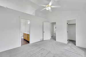 Unfurnished bedroom featuring lofted ceiling, ceiling fan, carpet flooring, a walk in closet, and ensuite bath